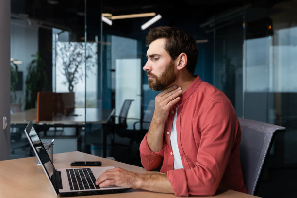 一个喉咙痛的男人在办公室里工作，一个商人在工作中有喉咙痛的流感和感冒，在工作中使用笔记本电脑图片下载