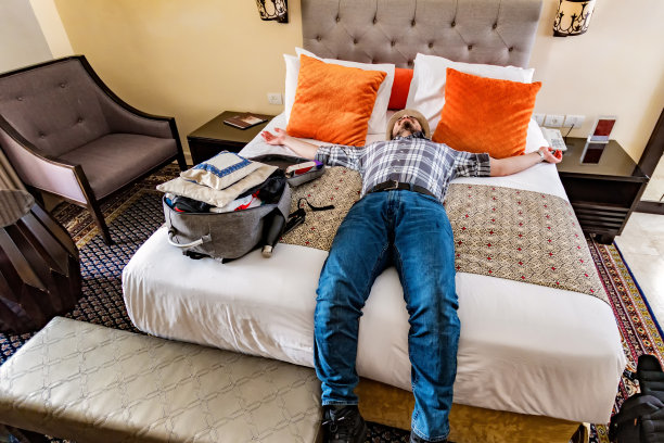 年轻的游客放松，躺在酒店房间的床上，张开双臂度假图片下载