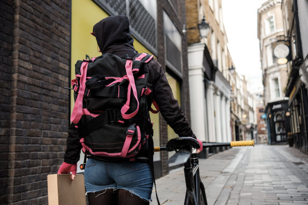 自行车快递员拿着包裹和她的自行车走路的背影。图片下载