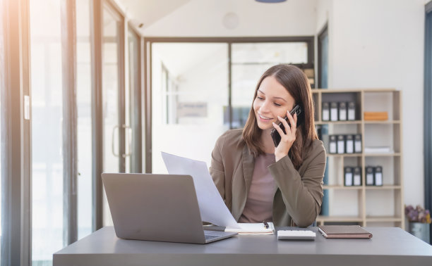 销售，财务，会计，计划，双语女商人正在与代表公司分销商的客户交谈，她在办公桌上用智能手机和笔记本电脑笔和记事本。图片下载