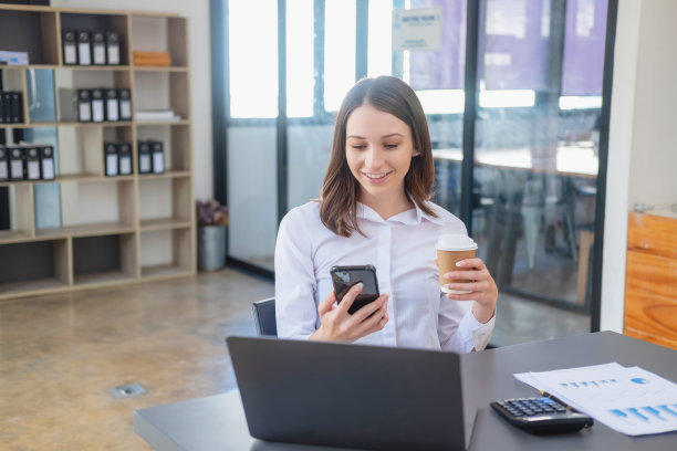营销，财务，会计，规划，白人混血女商人使用手机联系客户，通知他们公司的业务合作伙伴在办公桌上的笔记本电脑和文件。图片下载