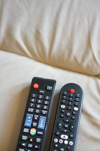 沙发上两个黑色塑料电视遥控器的选择性对焦镜头图片下载