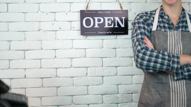 在零售商店或咖啡店工作的企业主或经理。企业家或员工站在开放的标志后面，准备为顾客服务或在咖啡馆点菜。概念小，创业起来。图片下载