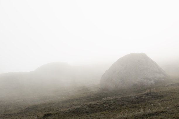 山区景观-轮廓的大灰色圆形石头在斜坡上在浓密的白色雾在朦胧的绿草的高山草甸在早期神秘的夏天早晨。达吉斯坦山区的旅游业。图片下载