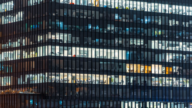 特写的办公大楼在晚上与一些轻的工作空间。现代的玻璃摩天大楼。金融区。在办公室工作到很晚。图片下载