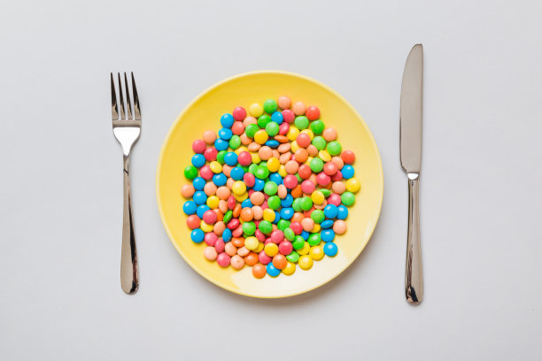 餐桌上有餐具，还有一盘糖果。健康和肥胖的概念，顶部视图的彩色背景图片下载