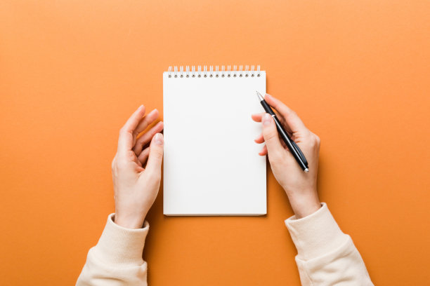 女人手里拿着铅笔在笔记本上写字。女人在办公桌旁工作。女性手握铅笔和速写本。模型的概念图片下载