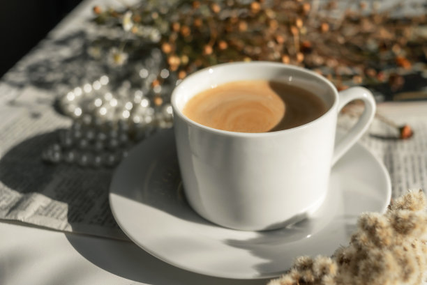 一杯白色的咖啡放在茶托上，上面有一串珍珠、干花、一本杂志和一份报纸。唯美的画面，优雅的背景照片。图片下载