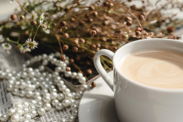 一杯白色的咖啡放在茶托上，上面有一串珍珠、干花、一本杂志和一份报纸。唯美的画面，优雅的背景照片。图片下载