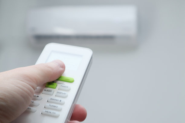 男人的手使用遥控器。手持遥控器和空调温度调节安装在白墙上。图片下载