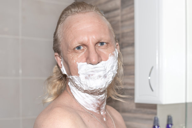 浴室里，一名脸上带着泡沫的成熟男子看着摄像头。早上刮胡子和卫生习惯图片下载