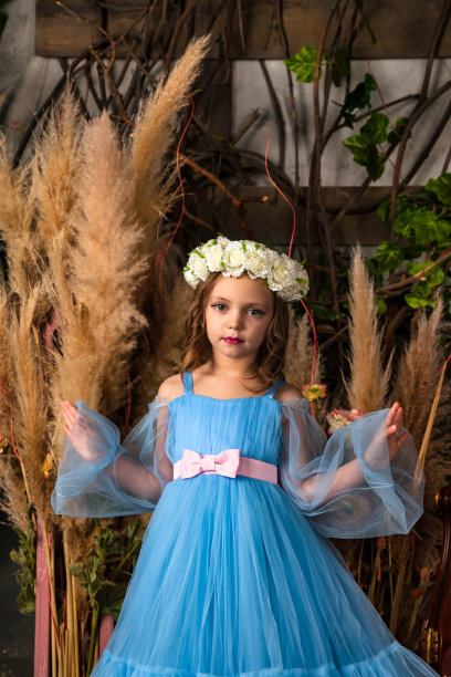 肖像小女孩公主摆着艺术浅蓝色连衣裙，头上戴着花环，站在神秘装饰的房间里，看着相机。幻想艺术照片，童话概念。本空间图片下载