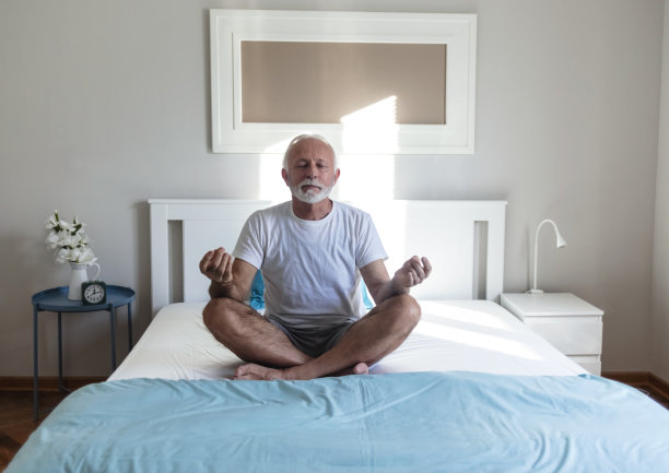 照片中，一位老人在床上醒来，得到了充分的休息。成熟男人醒来后在床上练习瑜伽。图片下载