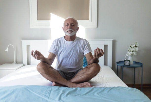 在家里醒来后，老年男子做早上瑜伽的剪裁镜头，坐在简单的姿势，sukhasana姿势和冥想。侧面视图的手在一个瑜伽的位置。图片下载