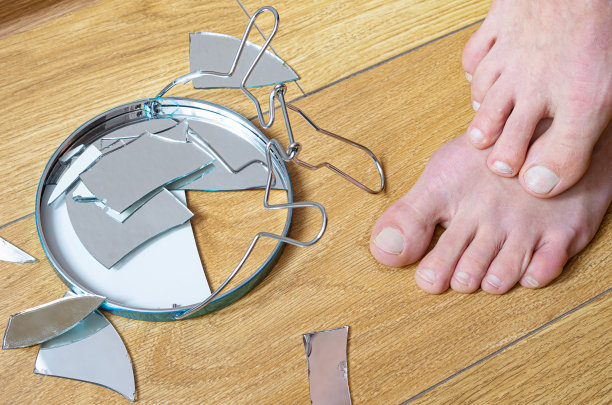 一位光着脚的妇女担心自己的腿会被家里木地板上的镜子碎片割伤图片下载