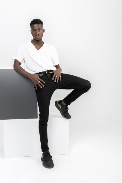 黑色英俊的非洲裔男子穿着白色衬衫，棕色织物裤子，黑色运动鞋与立方体在工作室。图片下载