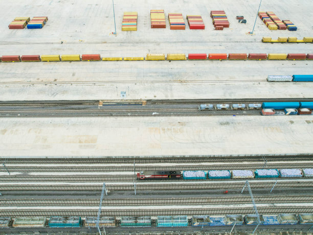 货运列车载着货运集装箱，背景中有成排的集装箱，无人机视图图片下载