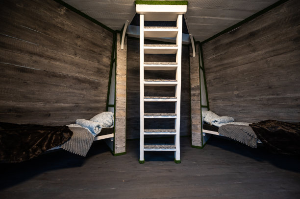 单人床和干净的亚麻布在小木屋的壁龛。金字塔形状的平房避暑别墅。倾斜的围墙，白色的楼梯，灰色的水平木板。非标准框架结构。图片下载