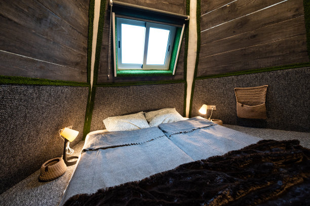 木屋卧室的双人床铺地毯。金字塔形状的平房。小房间，倾斜的墙壁，窗户灯，铺好的床。手工制作的木屋内部。图片下载