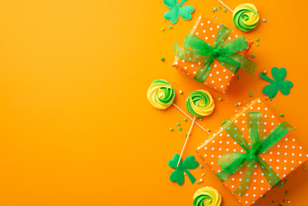 圣帕特里克节的概念。顶部视图照片的礼盒与绿色丝带蝴蝶结蛋白糖棒棒糖洒和三叶草在孤立的橙色背景与复制空间图片下载