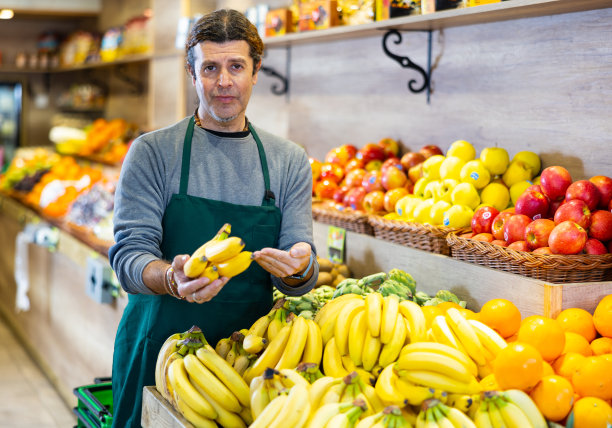 一名男子手持香蕉站在超市的水果和蔬菜区图片下载