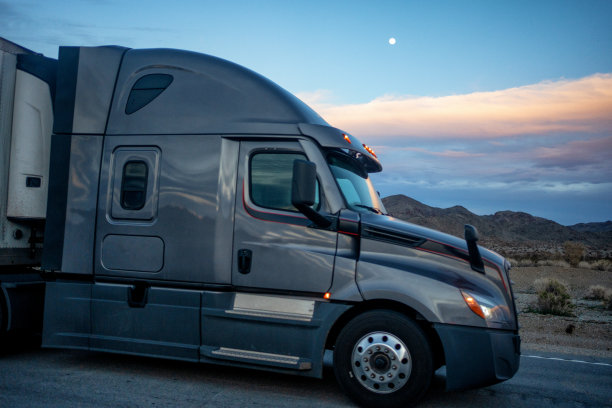 灰色的半卡车在一个美丽的夜晚穿过亚利桑那州的沙漠，在干旱的风景中，满月在山脉的背景上图片下载