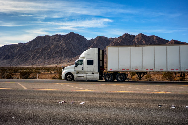 白色半卡车行驶在内华达州拉斯维加斯南部的一个阳光灿烂的日子里，在一个干燥干旱的景观中，山脉在背景中图片下载