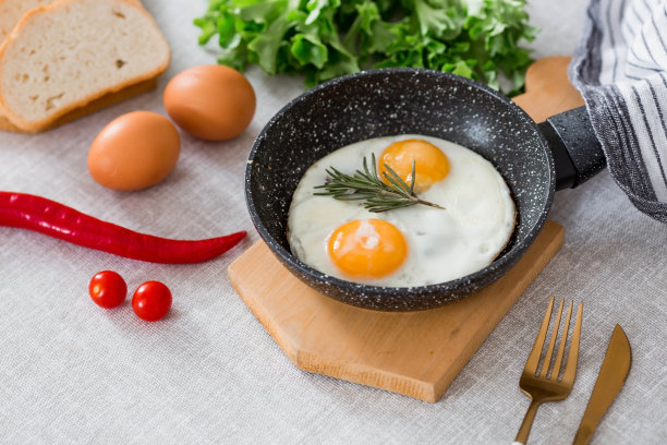 在平底锅里煎蛋，配上迷迭香、面包、鸡蛋和蔬菜沙拉，铺在亚麻桌布上。早餐，午餐和晚餐。视图是软的，选择性聚焦。乡村风格。图片下载