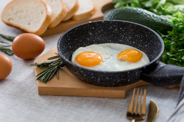 在平底锅里煎蛋，配上迷迭香、面包、鸡蛋和蔬菜沙拉，铺在亚麻桌布上。早餐，午餐和晚餐。视图是软的，选择性聚焦。乡村风格。图片下载
