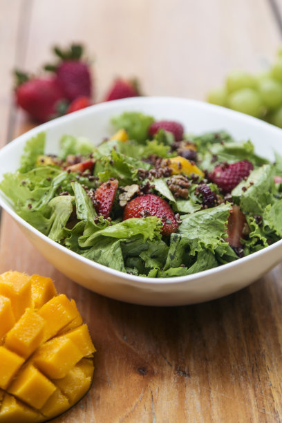 生菜，芒果，草莓，坚果和种子沙拉。盛在木桌上的白碗里。健康的一餐。图片下载