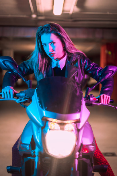 一名身着皮夹克的西班牙女子在霓虹灯下的摩托车上摆造型图片下载
