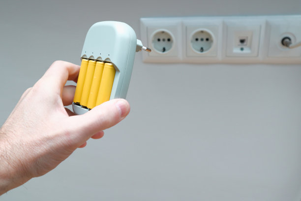 充电器和电池在人的手中。男性手持充电器与黄色AA电池，白色背景与插座图片下载