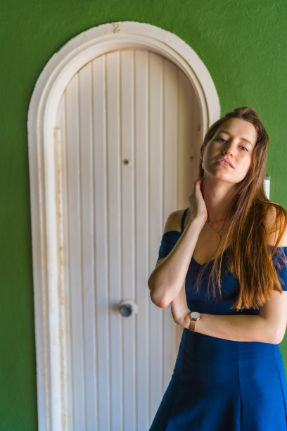 年轻迷人的红头发，来自西班牙，穿着蓝色连衣裙，站在一座绿色建筑的白色木门旁图片下载