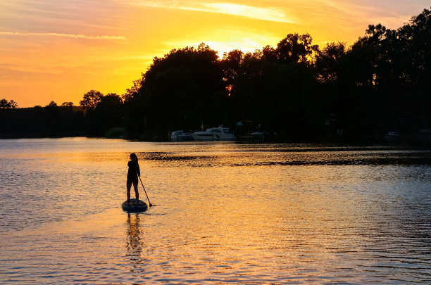 在日落或日出时，女孩在美丽的湖泊上划桨，站在德国湖区梅克伦堡的早晨冒险图片下载