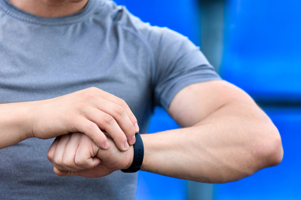 身穿灰色t恤的运动员双手肌肉发达，正在看智能手表上的时间图片下载