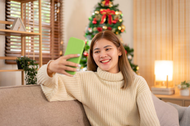 年轻的亚洲女子穿着毛衣，微笑着坐着放松，用智能手机拍照图片下载