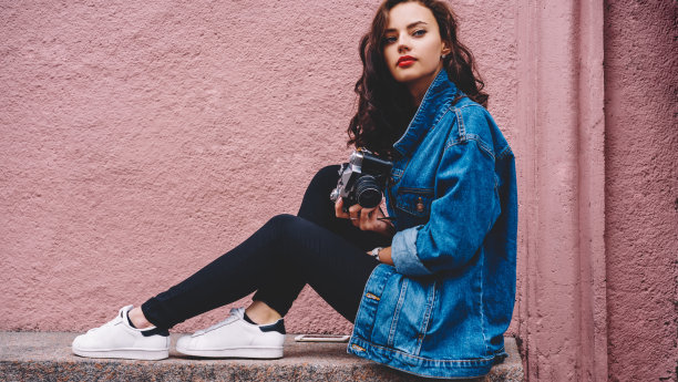 时尚年轻的女摄影师坐在破旧的石头表面图片下载