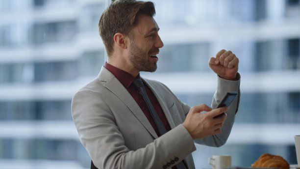 专业人士在咖啡馆办公室用手机阅读好消息庆祝胜利。图片下载