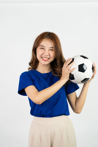 快乐的亚洲女球迷穿着蓝色衬衫为喜爱的球队加油，白色背景上孤立的足球，年轻漂亮的女孩抱着足球，运动概念图片下载