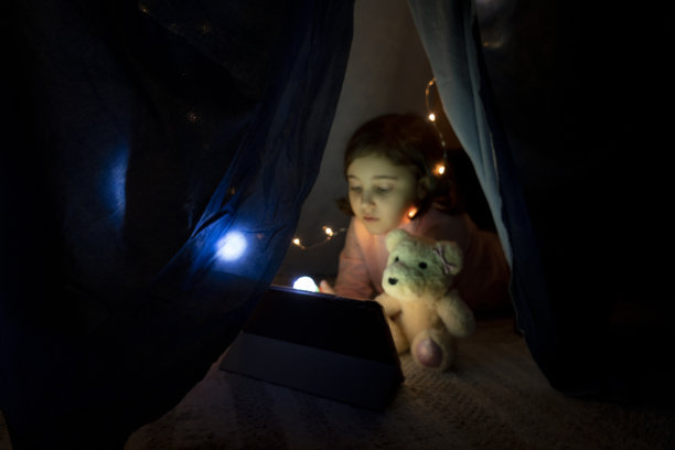 小女孩晚上在卧室的帐篷里用平板电脑看书图片下载