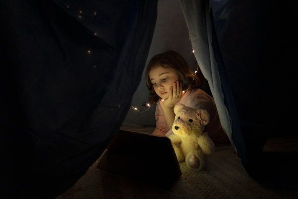 小女孩晚上在卧室的帐篷里用平板电脑看书图片下载