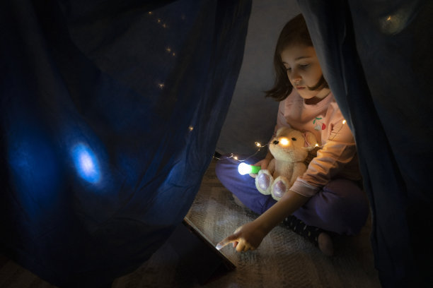 小女孩晚上在卧室的帐篷里用平板电脑看书图片下载