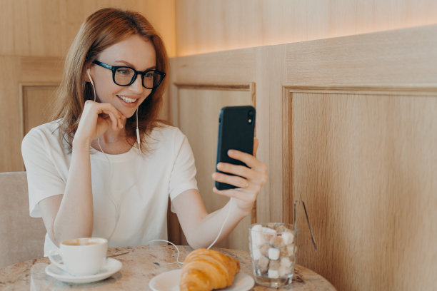 室内照片，一名开朗的红发年轻女子使用手机和耳机进行在线交谈图片下载