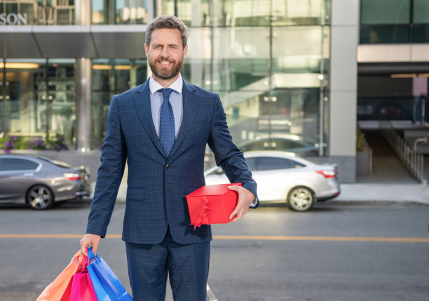 快乐的成功商人穿着正装，带着购物袋走在户外，做生意。图片下载