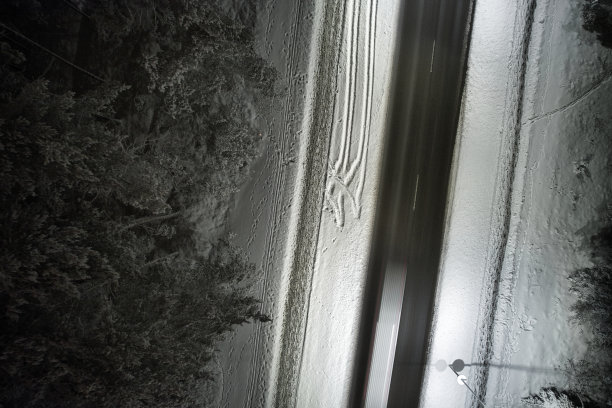 无人机拍摄的冬季道路在夜间蜿蜒穿过积雪覆盖的森林在山上图片下载