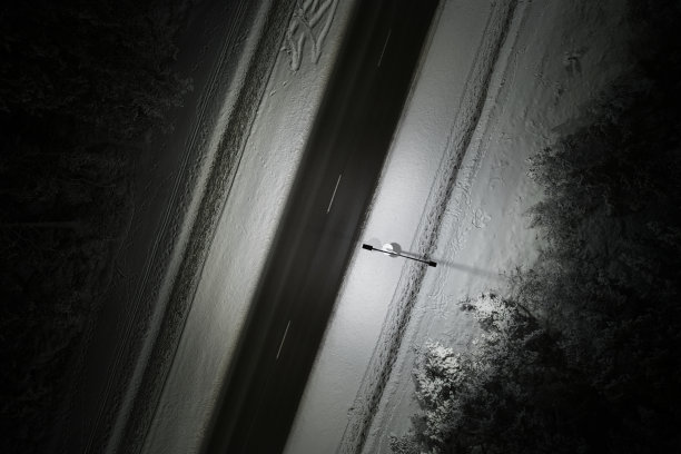 无人机拍摄的冬季道路在夜间蜿蜒穿过积雪覆盖的森林在山上图片下载