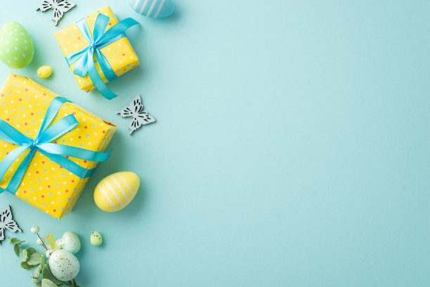 复活节庆祝概念。俯视图照片生动的黄色礼盒与蓝色丝带蝴蝶结花束与彩色复活节彩蛋和蝴蝶在孤立的浅蓝色背景与空白图片下载
