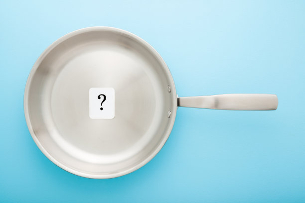 不锈钢煎锅，浅蓝色桌子背景上有黑色问号的白色卡片。特写镜头。柔和的颜色。烹饪概念。自顶向下视图。图片下载