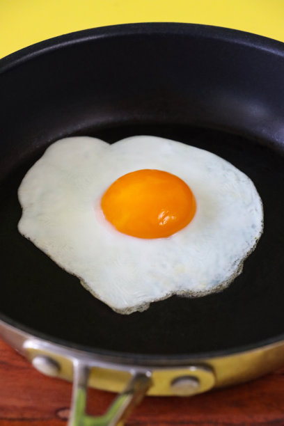 在不粘锅里煎蛋的全帧图片，阳光面朝上，黄色背景，高视图，重点在前景图片下载