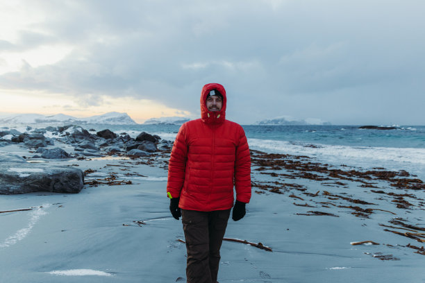 一名穿着红色夹克的男子在挪威风景优美的海滩上凝视着冬日的日落图片下载